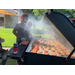 A couple people standing and cooking at an outdoor grill filled with food.
