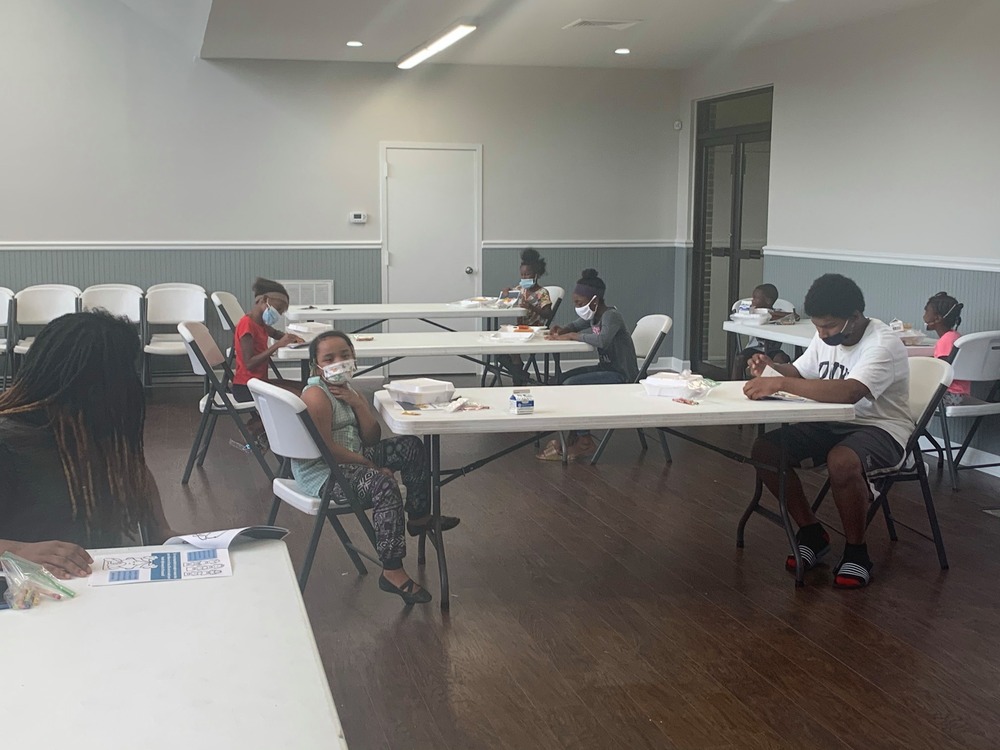 The after-school program students in the Harris Gardens Community Room sitting at tables wearing masks.