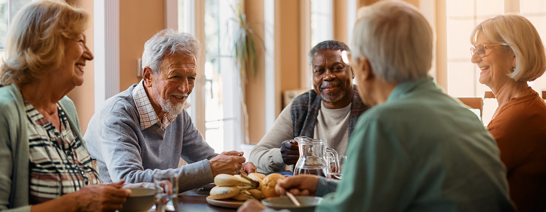 A group of men and women sitting around a table smiling at each other.